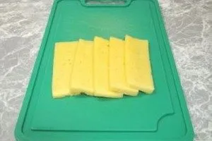 Сыр нарезать длинноватыми пластинками так, чтобы его удобно было заворачивать в тесто вместе с сосиской.