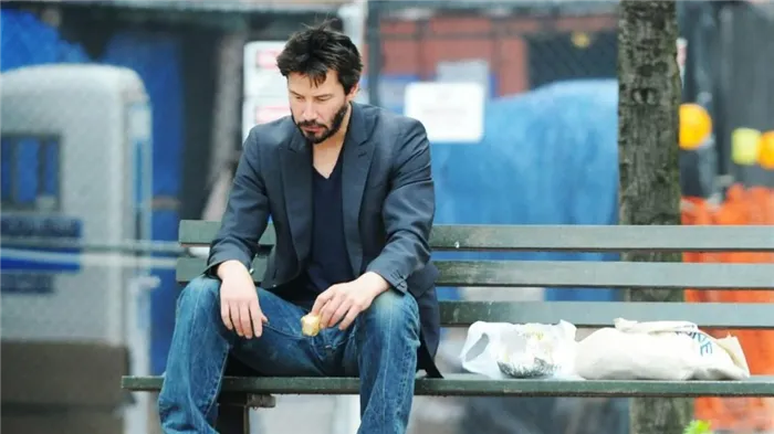 Актер Киану Ривз грустный силит на лавочки и ест бутерброд
